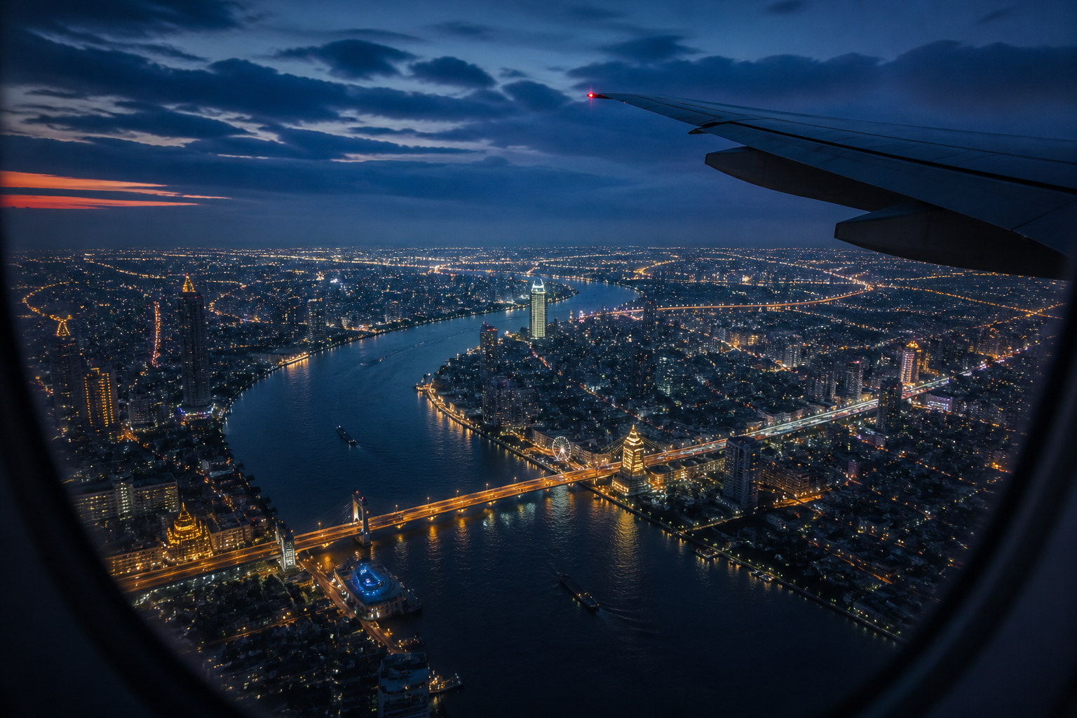 Airplane wing above Bangkok and its river at blue hour
